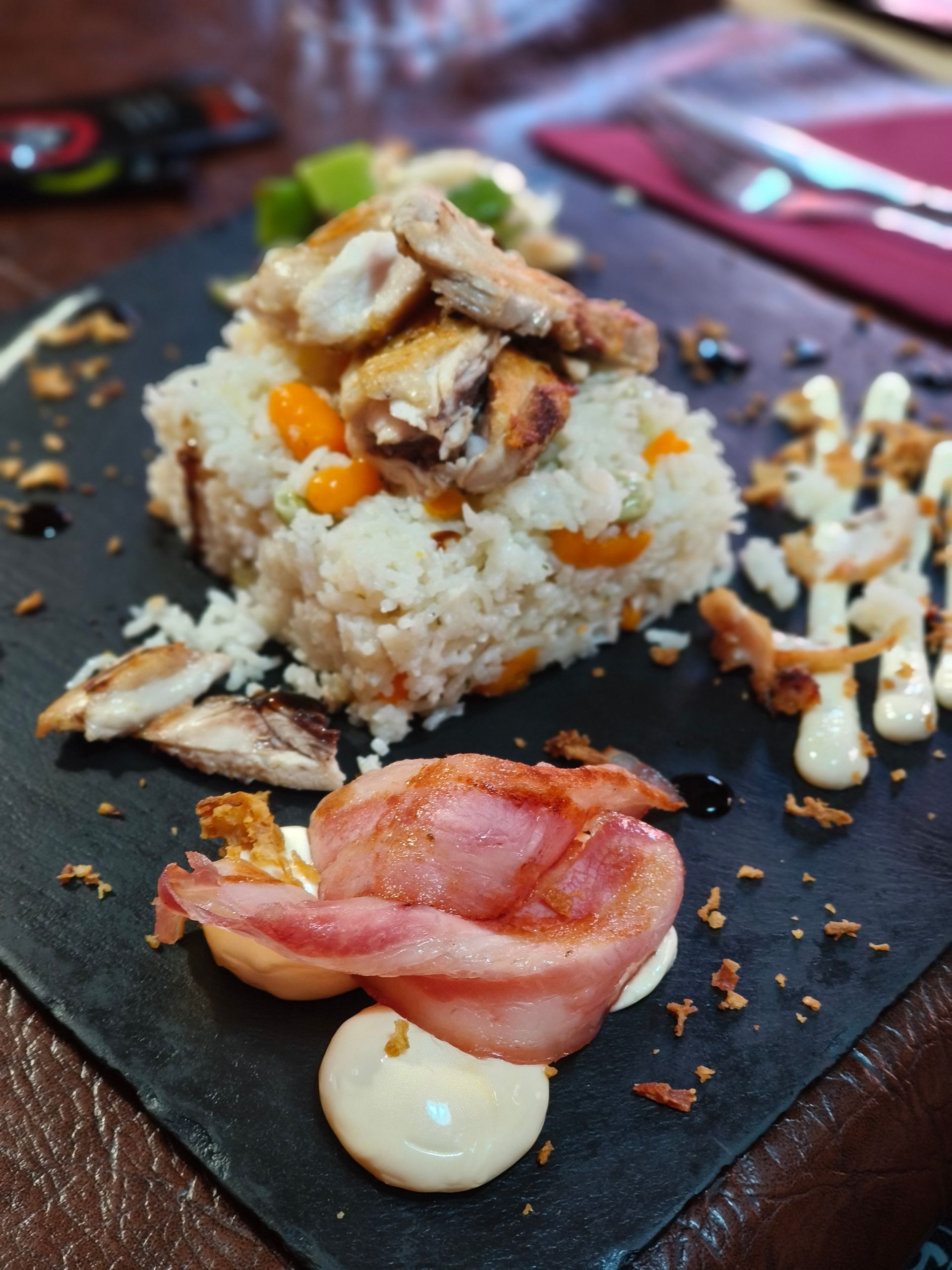 Un plato de comida con arroz y tocino en una mesa.