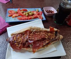 Un sándwich está sobre un plato blanco sobre una mesa al lado de un plato de tomates y aceitunas.
