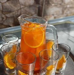 Una jarra de jugo de naranja está rodeada de vasos llenos de rodajas de naranja.