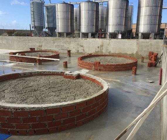 Tres estructuras de hormigón rodeadas de ladrillos sobre una superficie plana, con grandes tanques al fondo.