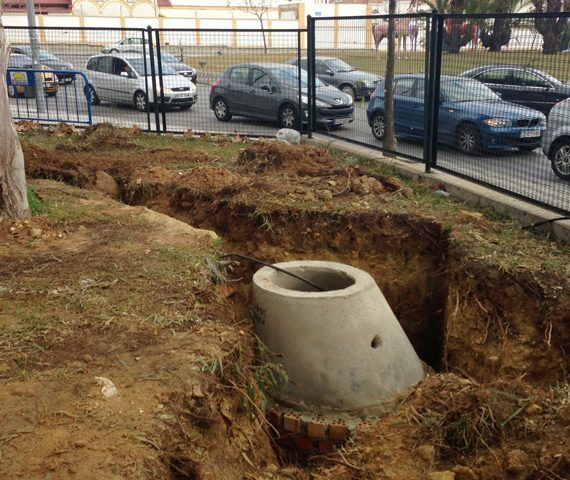 Tubería de drenaje de hormigón en una excavación al borde de la carretera; automóviles circulando al fondo.