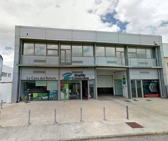 Edificio comercial de dos plantas con varias tiendas. Exterior blanco y gris con cielo nublado.