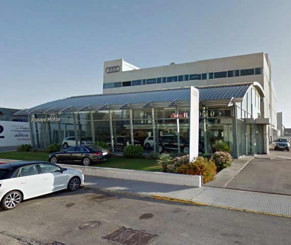 Concesionario Audi con fachada de cristal donde se exhiben los coches; el edificio tiene exterior gris y blanco.