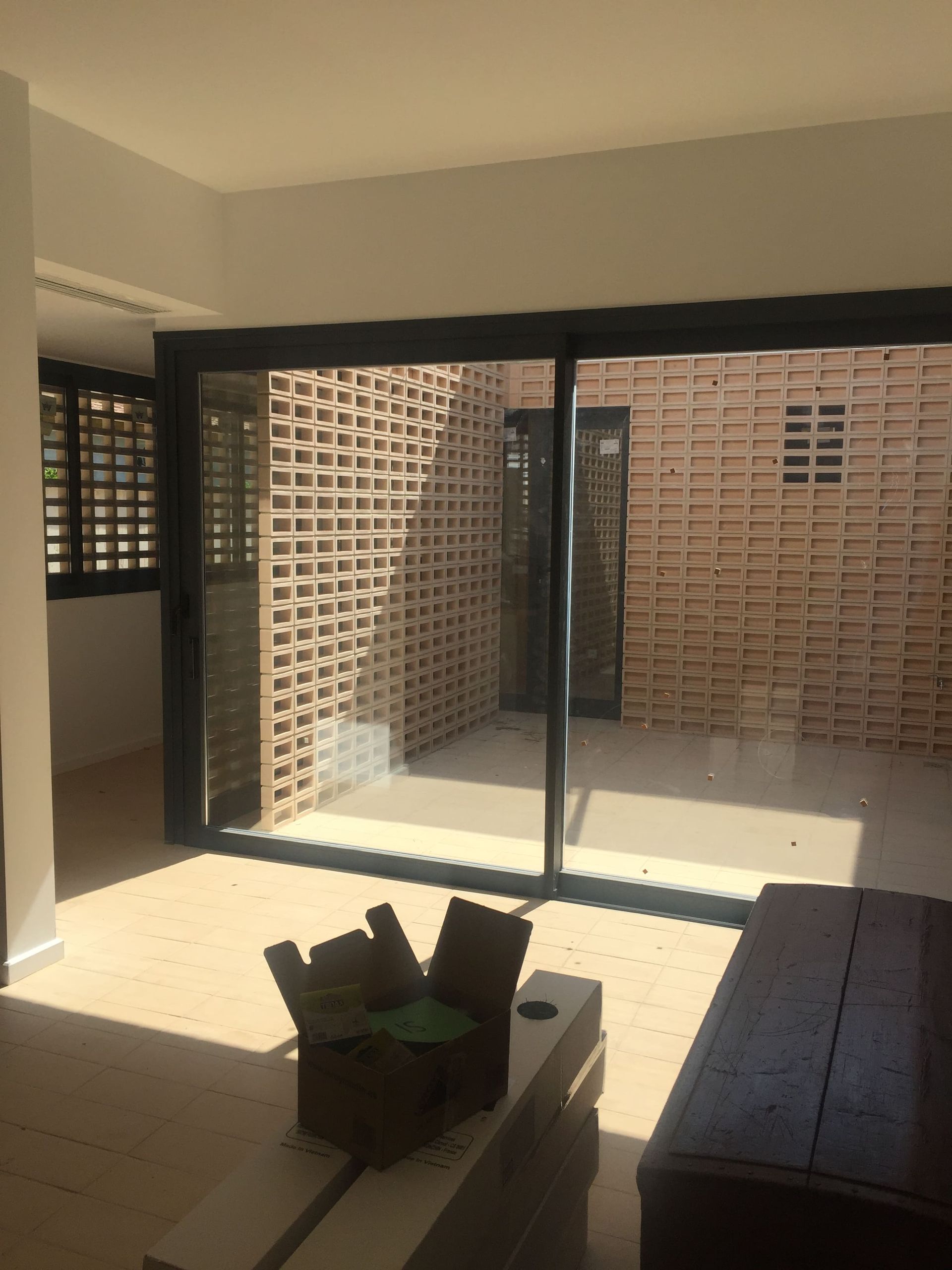 Interior con puertas corredizas de vidrio abiertas a un patio de ladrillo; una mesa de café de madera en primer plano.