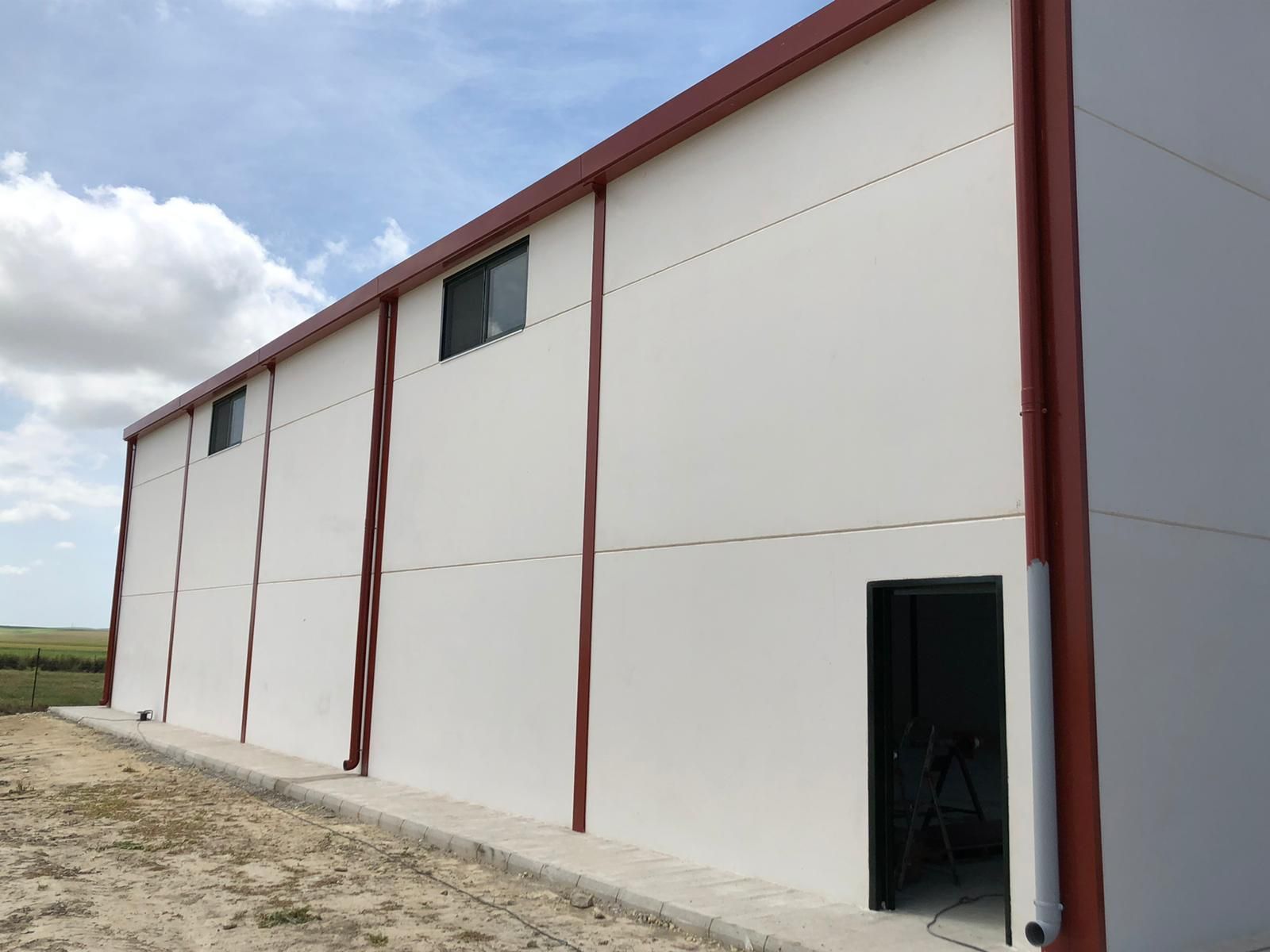 Edificio industrial blanco con detalles rojos, ventanas y puerta abierta en un día soleado.