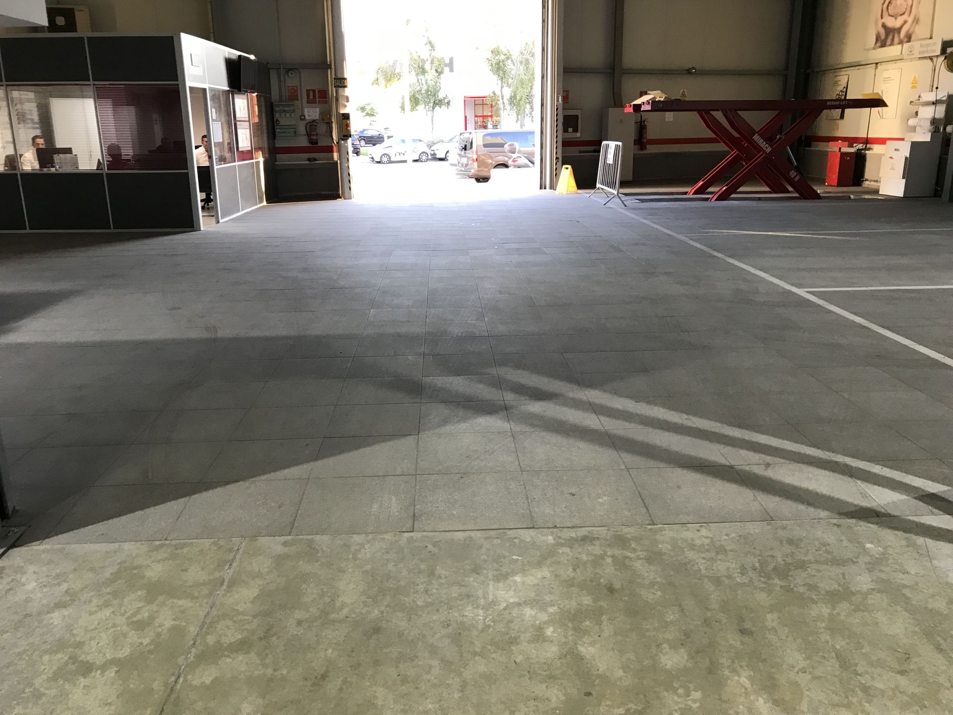 Un piso amplio, plano y gris en el interior de un garaje conduce a una puerta abierta con vehículos visibles.
