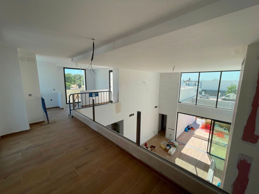Vista interior de una casa moderna en construcción; espacio abierto con grandes ventanales y pisos de madera.