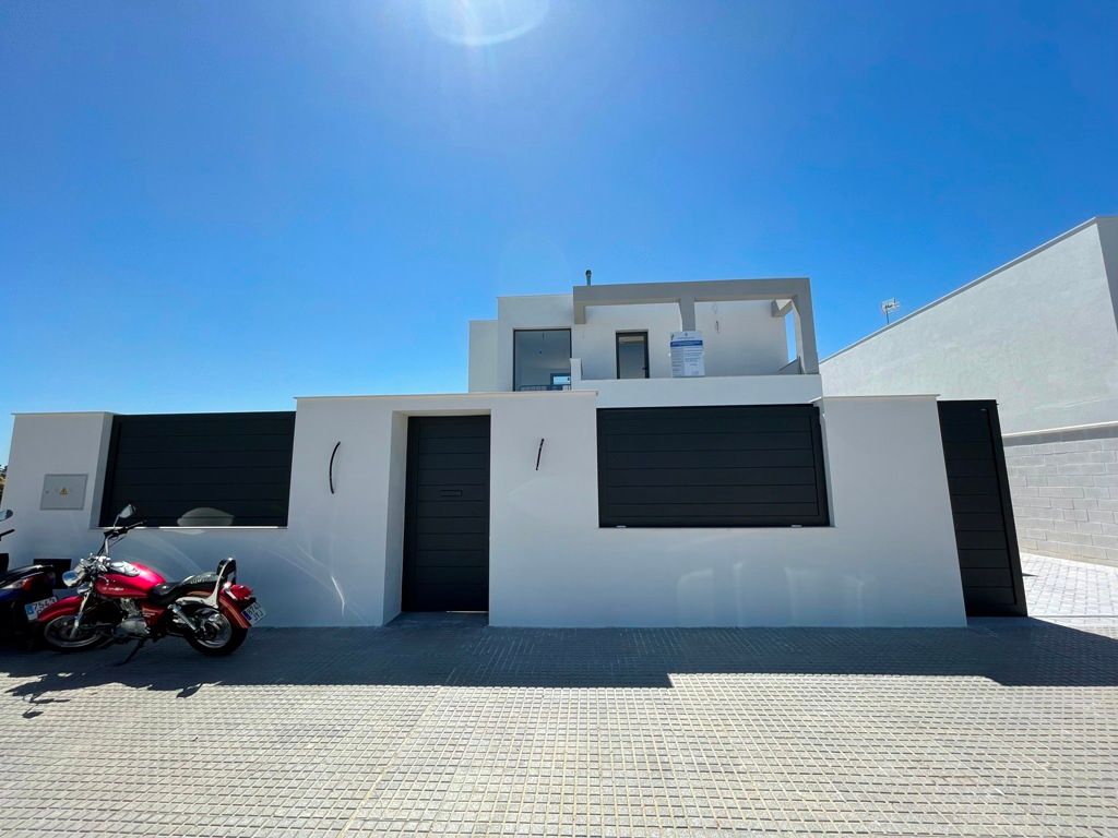 Casa moderna de color blanco con puerta y persianas de color gris oscuro; motocicleta estacionada en frente.