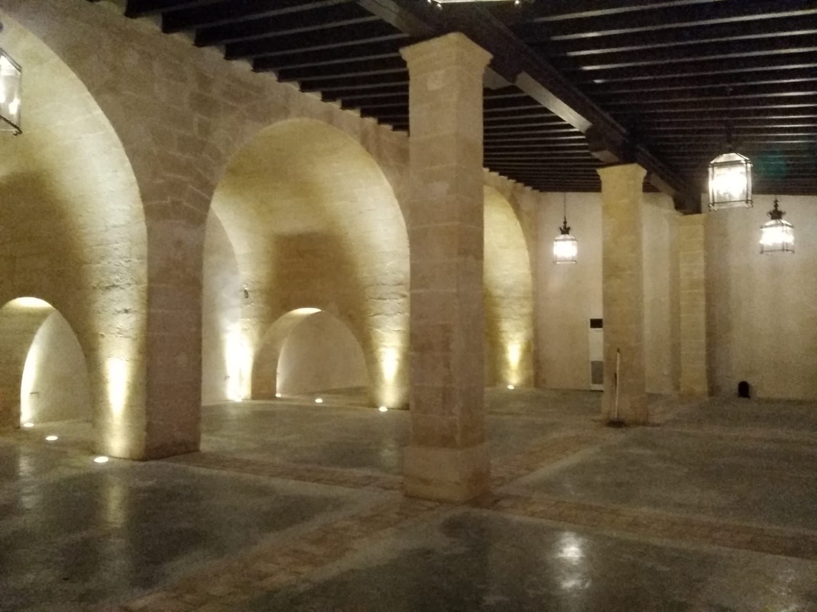 Interior de piedra con techos abovedados, pilares y faroles colgantes.