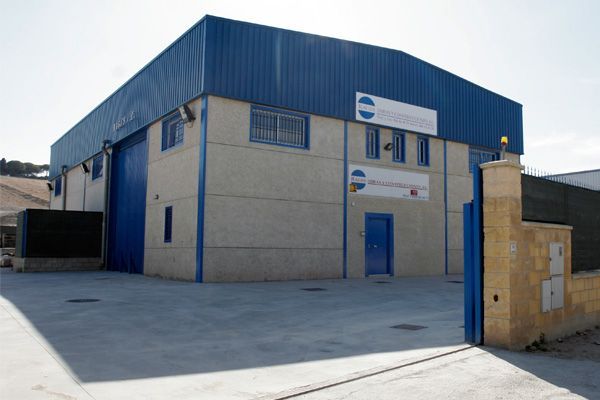 Nave industrial con puertas y tejado azules, logo en la fachada y portón abierto.