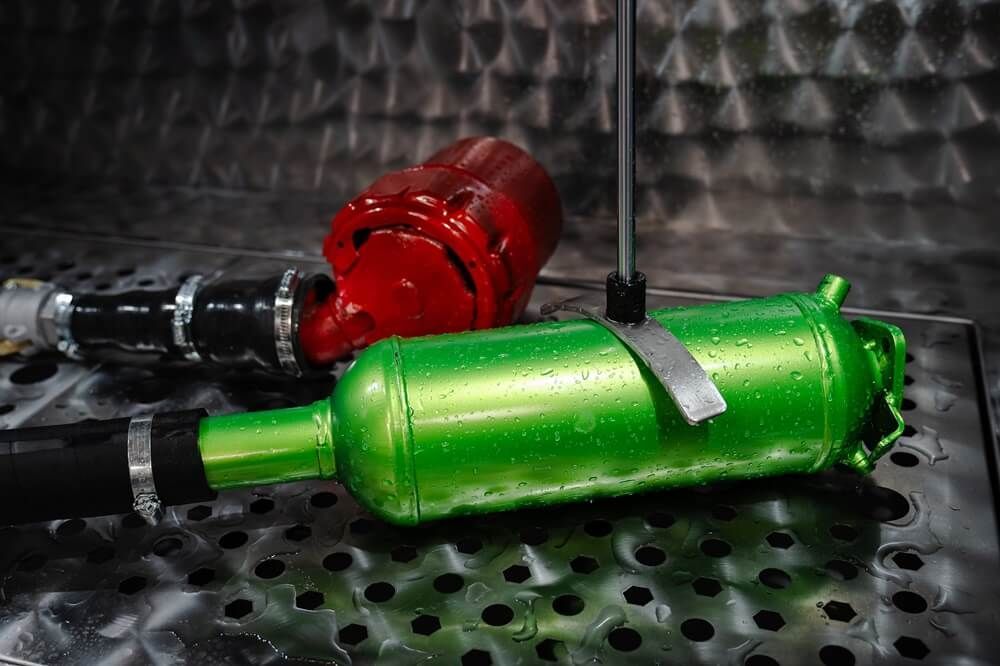 A green bottle and a red bottle are sitting on a metal surface.