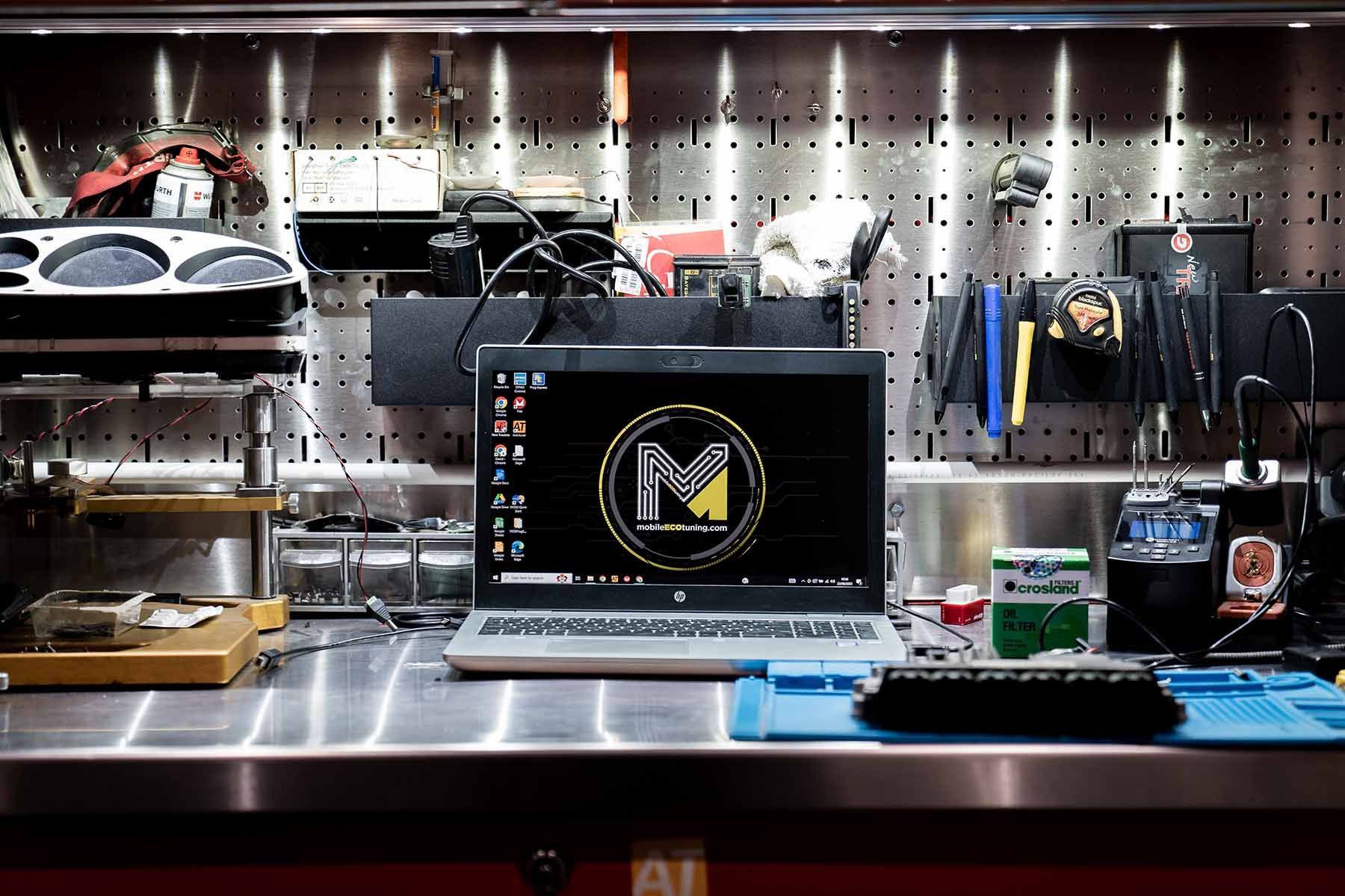A laptop with the letter m on the screen is sitting on a workbench.
