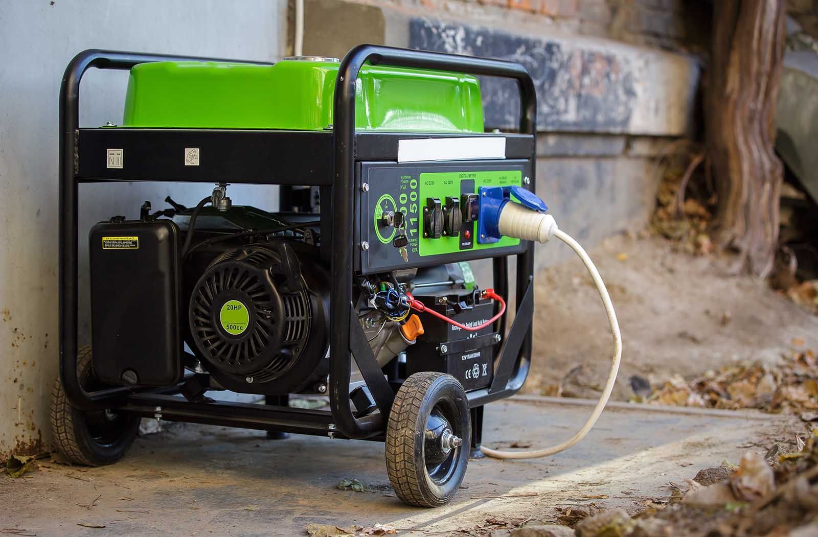 A green and black generator is plugged into a wall.