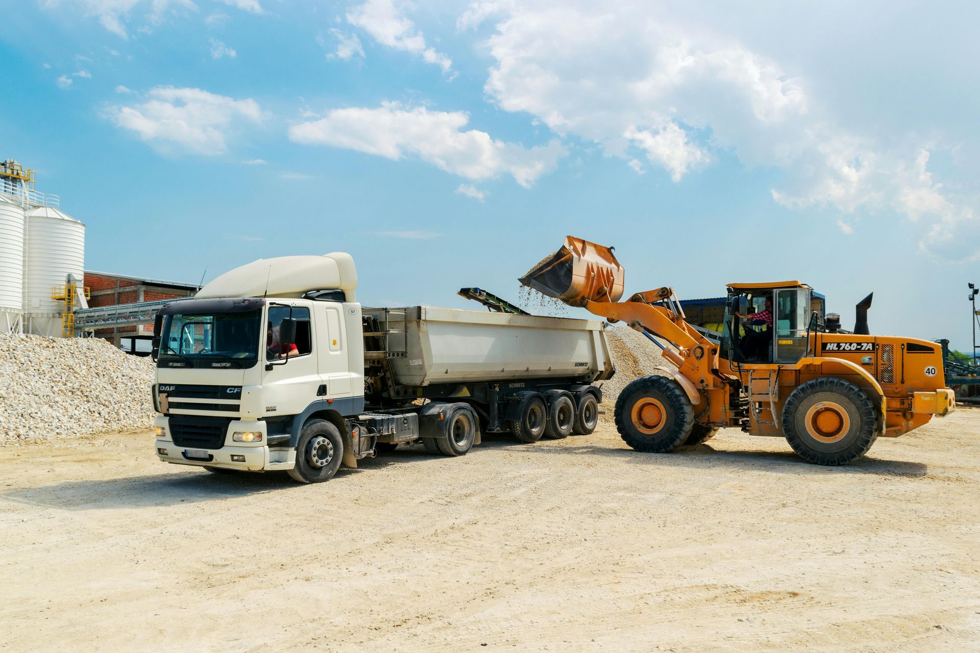 A dump truck is being loaded with sand by a bulldozer.