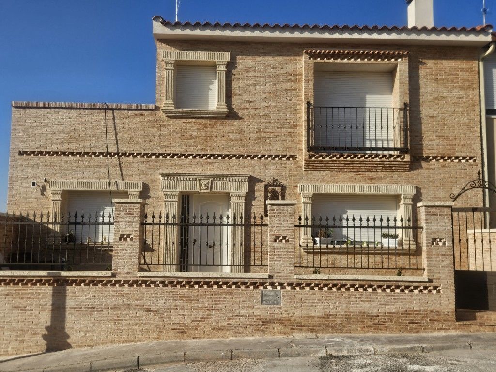 Casa de ladrillo de dos plantas con balcones y barandillas de hierro forjado bajo un cielo azul.