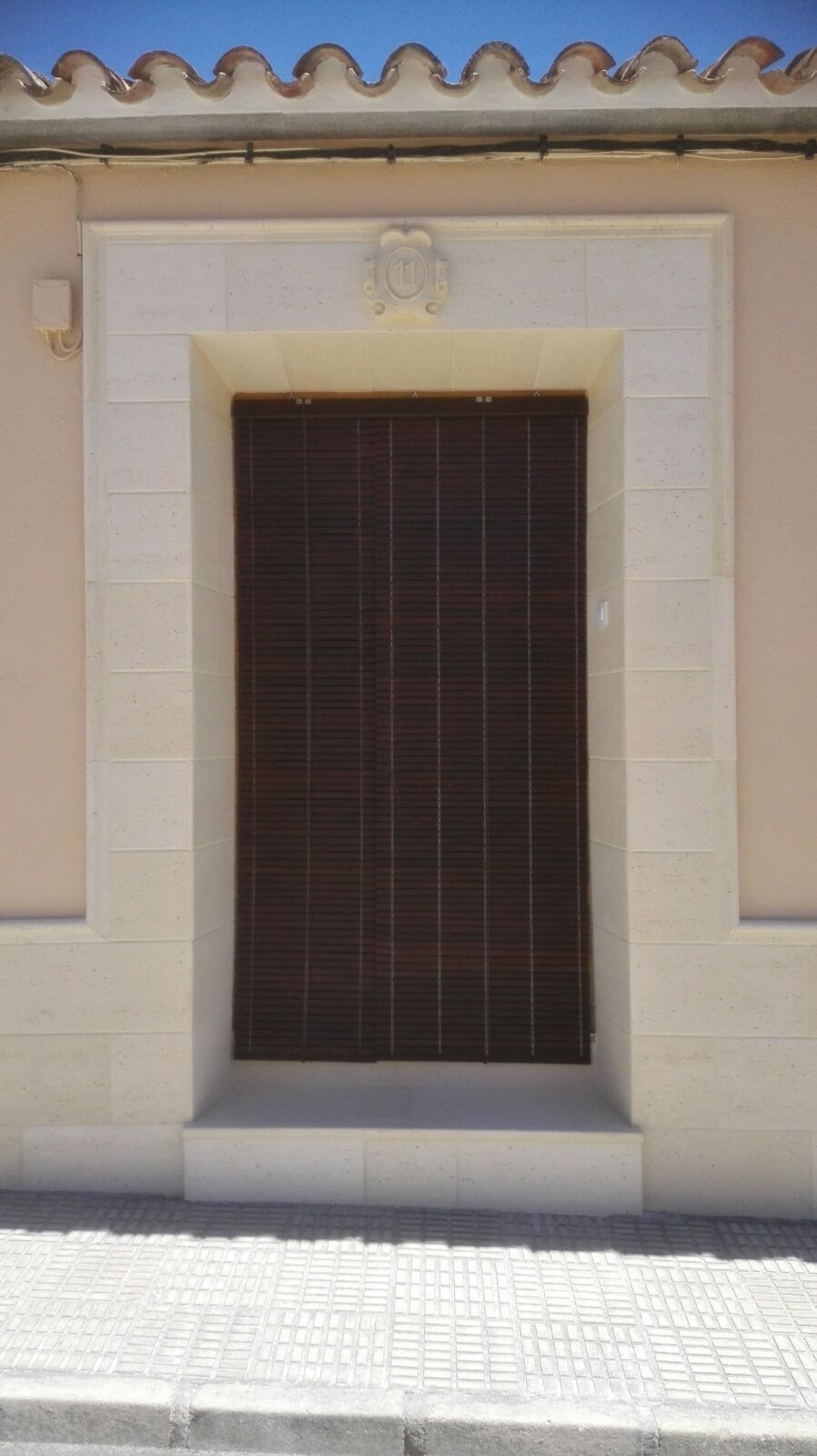 Puerta cerrada de madera oscura en una pared de estuco color crema con remate de teja en el tejado.