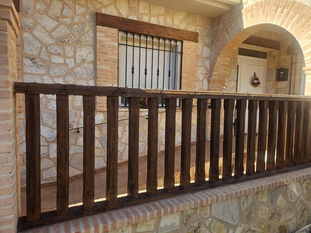Balcón de piedra en el patio con barandilla de madera oscura y ventana arqueada.