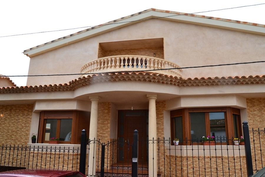 Vista frontal de una casa de estuco beige con balcón, porche arqueado y valla de hierro negro.