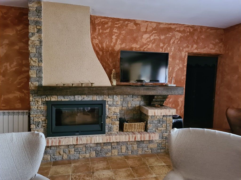 Chimenea en la sala de estar con revestimiento de piedra, televisor sobre la repisa y pared texturizada de color naranja.