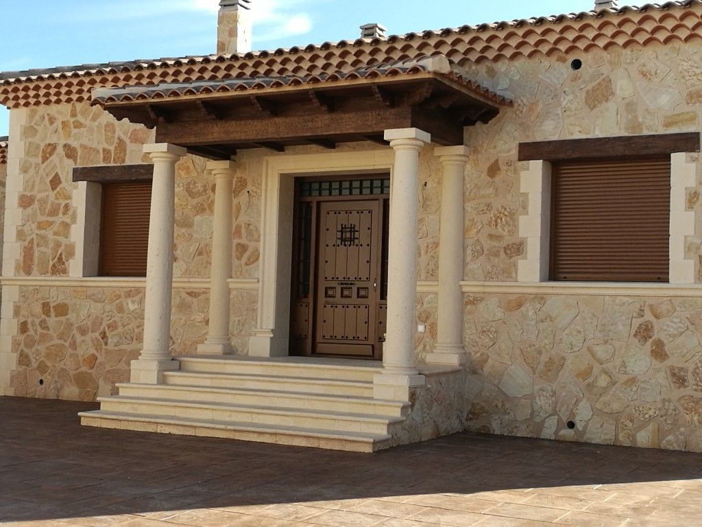 Fachada de casa de piedra con puerta de madera, dos columnas, contraventanas y tejado de tejas.
