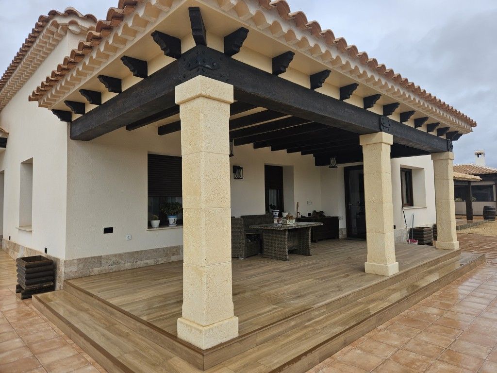 Patio cubierto con columnas de piedra y vigas de madera en la terraza de una casa.