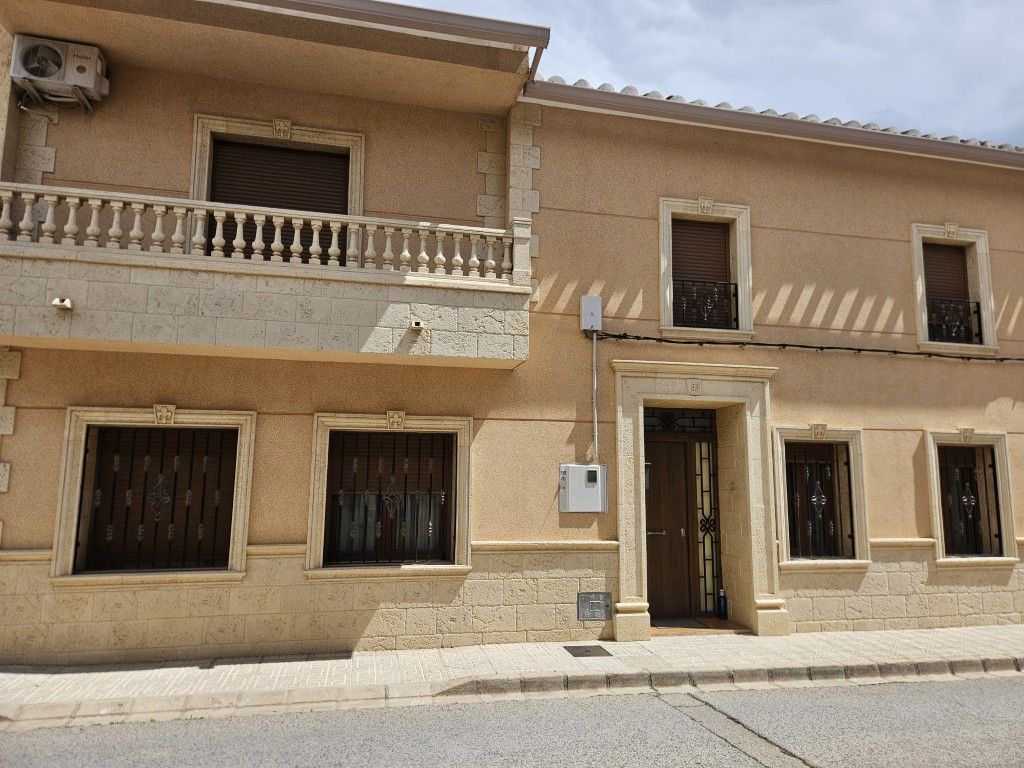 Fachada de casa de estuco color canela con balcón, ventanas enrejadas y una puerta central en una calle tranquila.