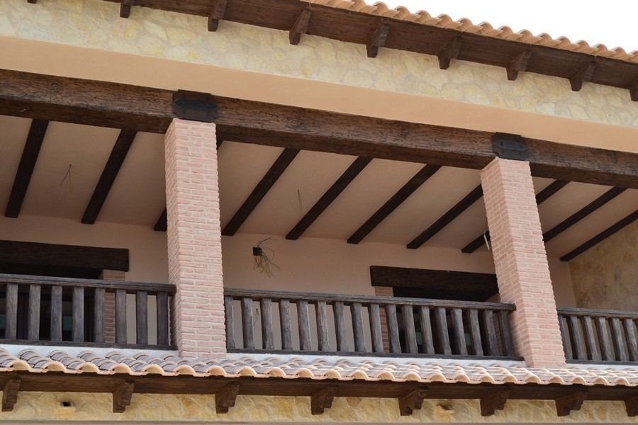 Balcón exterior con vigas de madera, columnas de ladrillo y detalles de techo de tejas.