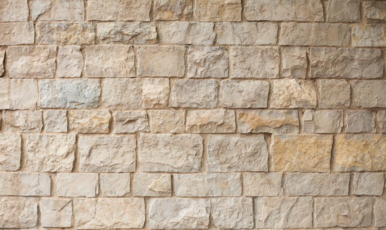 Primer plano de un muro de piedra beige con bloques de mampostería rectangulares.
