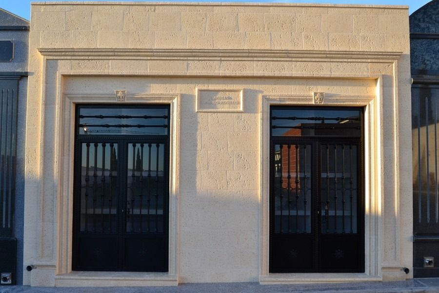 Fachada moderna de color beige con dos grandes puertas y ventanas de cristal con marcos negros.