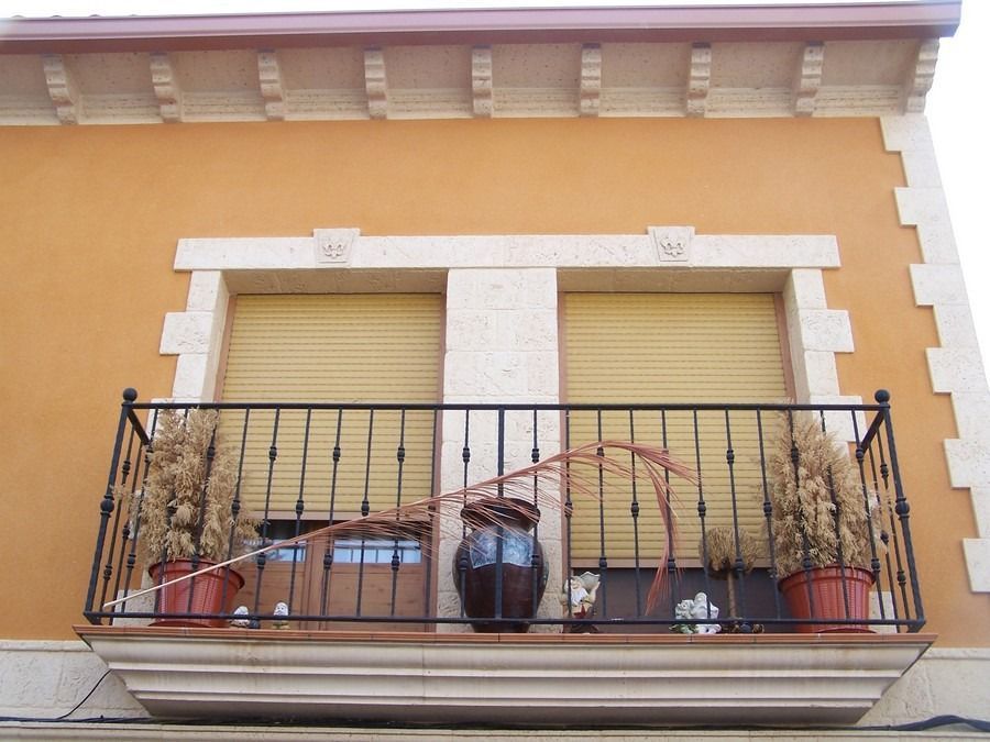 Fachada naranja del edificio con dos contraventanas cerradas y un balcón de hierro forjado con macetas.