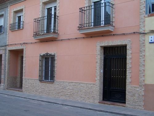 Edificio de estuco rosa con ventanas enrejadas y una puerta negra en una calle estrecha.