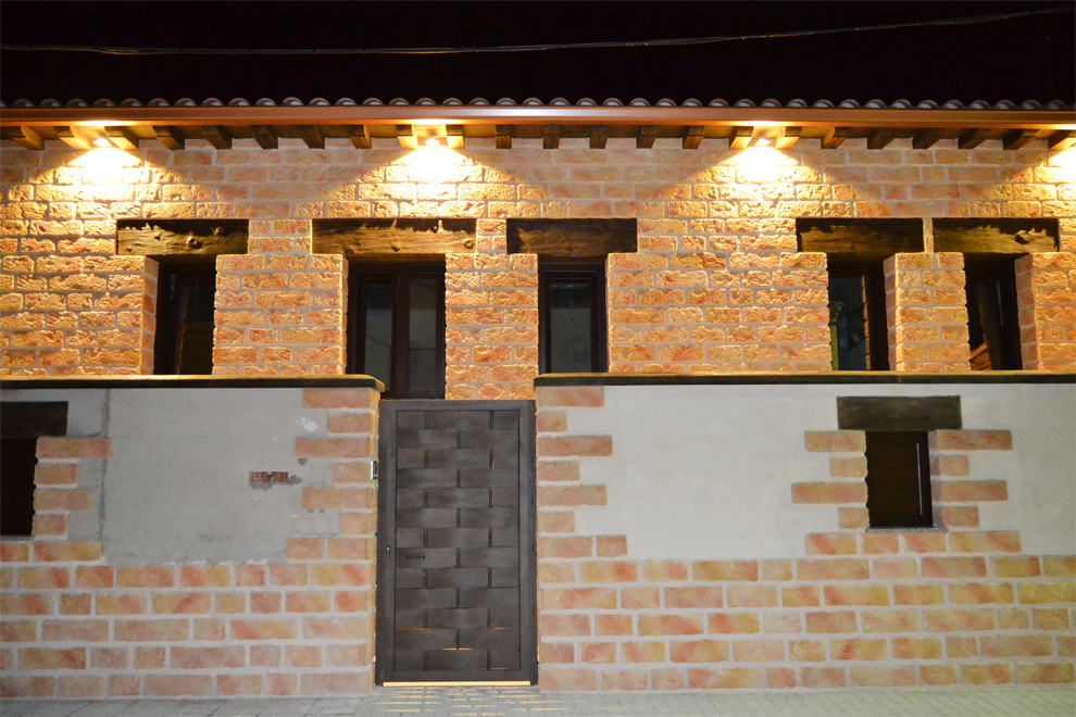 Fachada de ladrillo de una casa por la noche con luces exteriores encendidas y una puerta principal centrada.