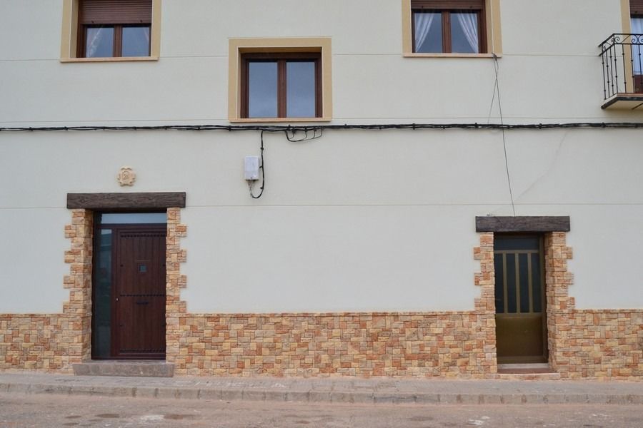 Un edificio de estuco blanco con dos puertas de madera, ventanas en la parte superior y mampostería en la parte inferior.