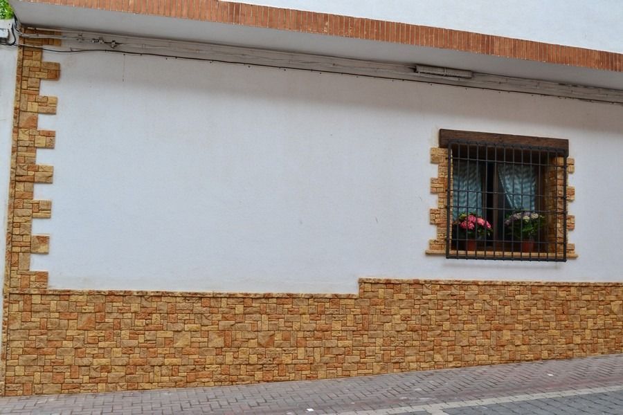 Muro blanco del edificio con detalles de ladrillo y una pequeña ventana con jardineras.