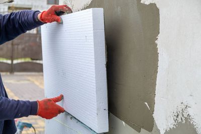 Arbeiter montiert weisse Schaumstoff-Dämmplatten an einer Aussenwand mit grauem Putz.