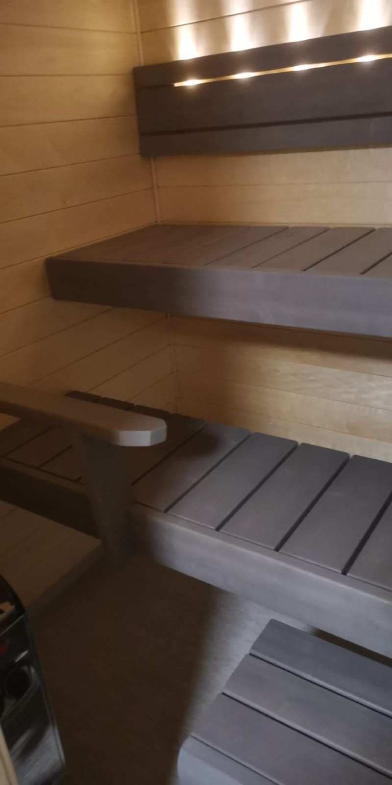 Sisäkuva saunasta, jossa on puiset penkit ja seinät. Valo paistaa ylhäältä.