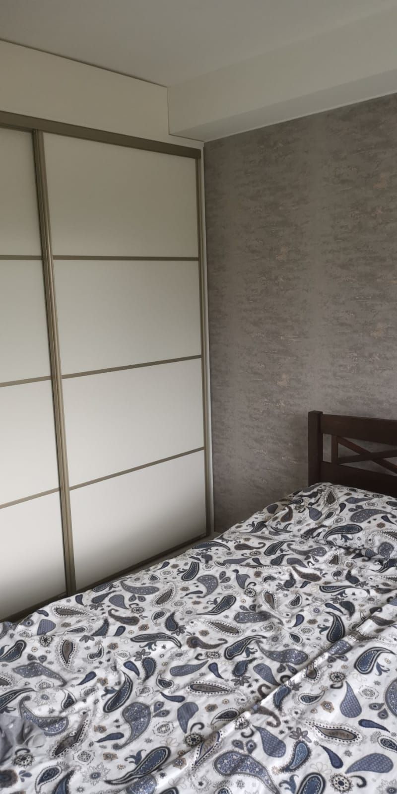 Makuuhuone, jossa on sänky ja suuri liukuovinen vaatekaappi. Seinät ovat harmaat ja päiväpeitto on kuviollinen.