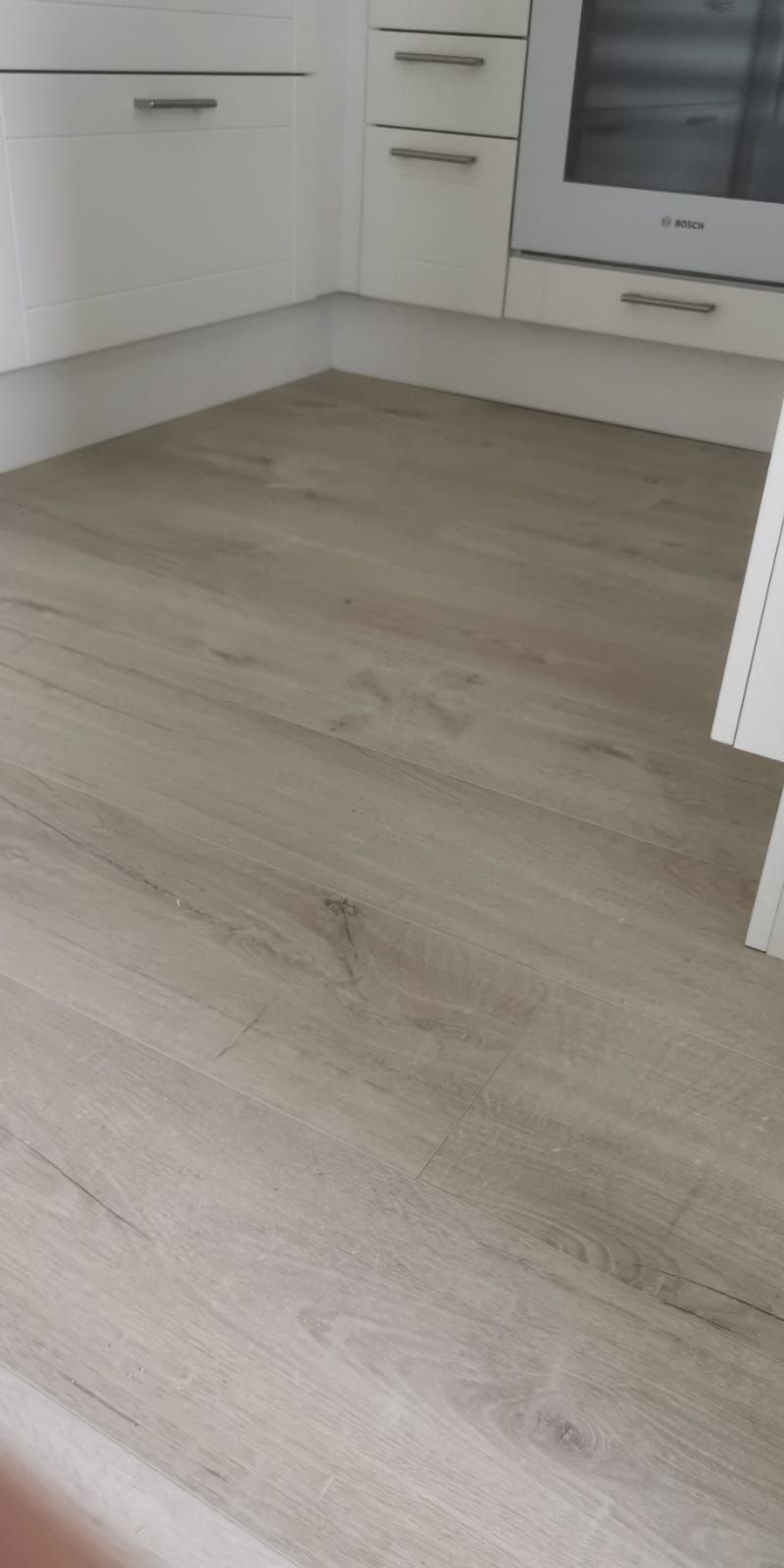 Puulattia keittiössä, jossa on valkoiset kaapit ja uuni.