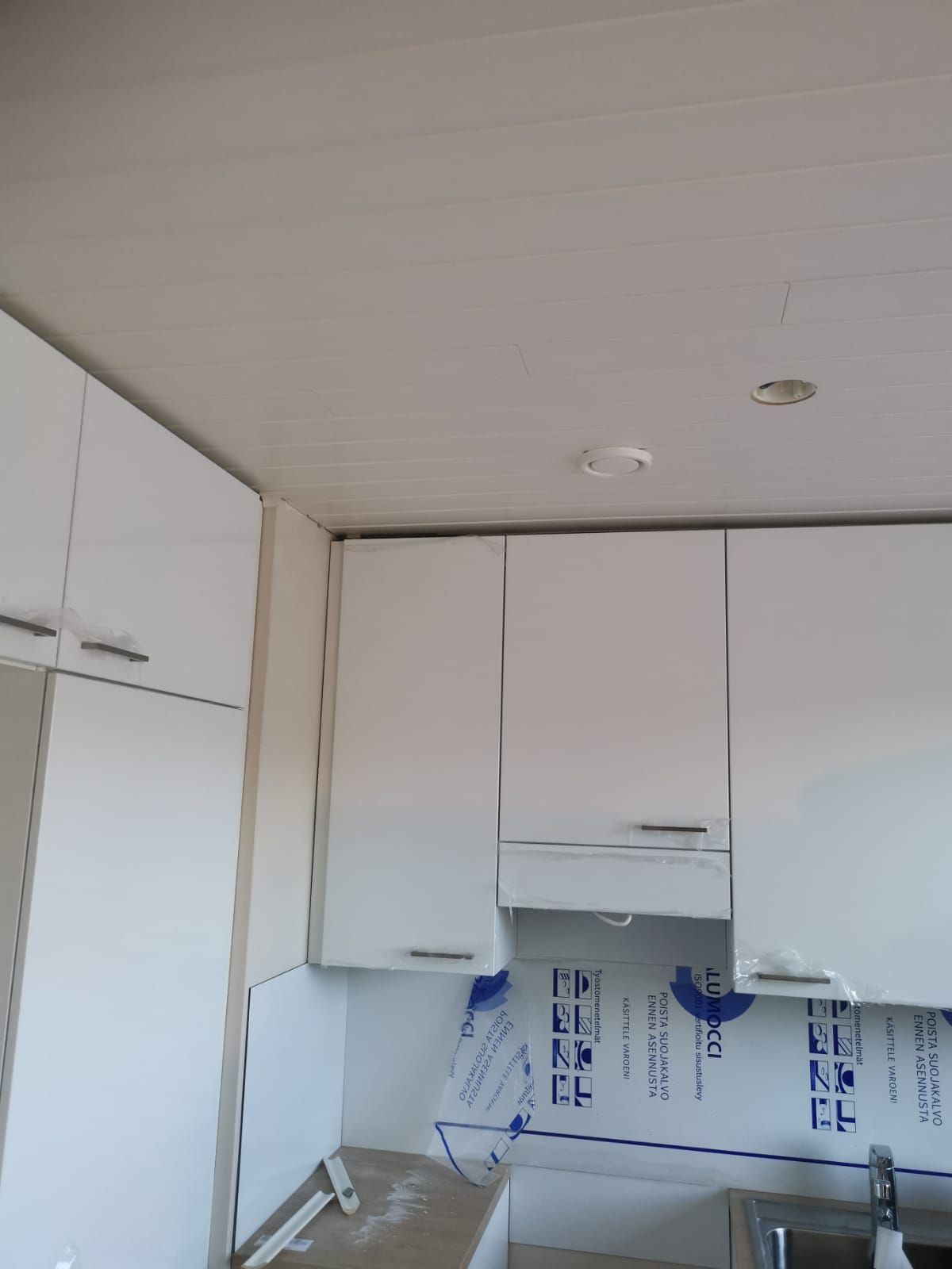 Valkoiset keittiönkaapit valkoista kattoa vasten, osittain asennettuina.