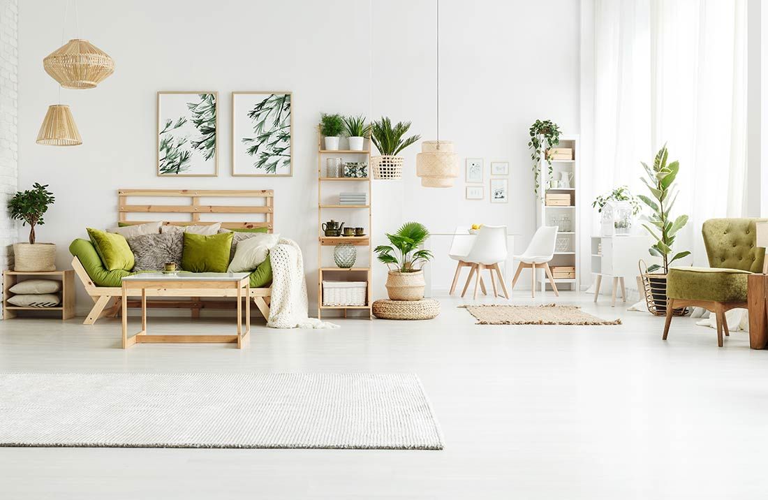 Kirkas olohuone, jossa puiset huonekalut, kasvit ja valkoiset seinät luovat viihtyisän ja luonnollisen tunnelman.