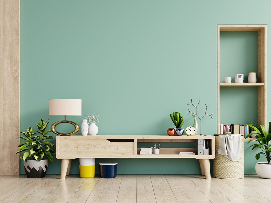 Mintunvihreä seinä, jossa puinen konsolipöytä, kasveja, hyllyjä ja lamppu.