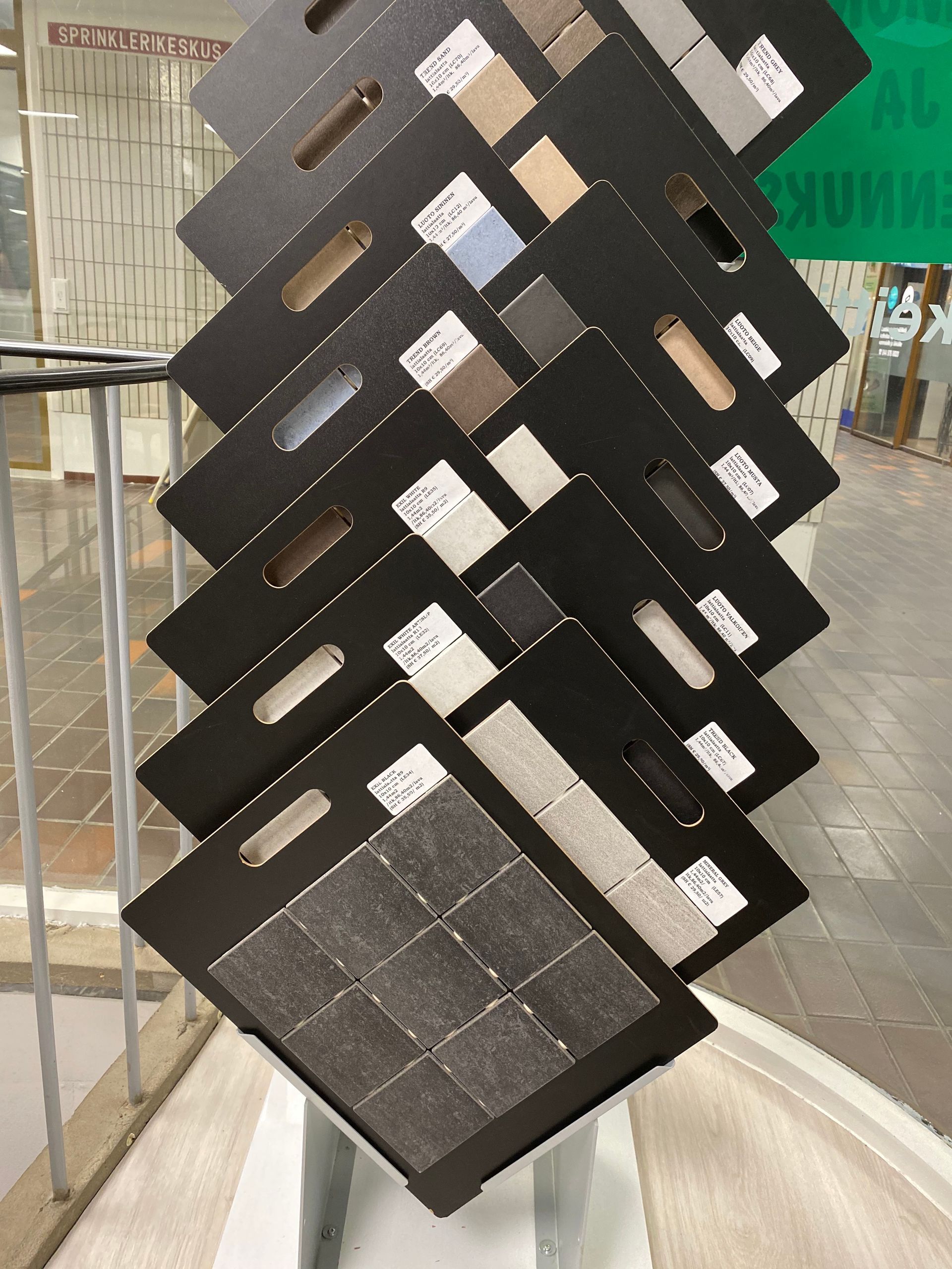 Kallistetuilla mustilla paneeleilla varustettu esittelyteline, jossa esitellään erilaisia kivilaattanäytteitä.