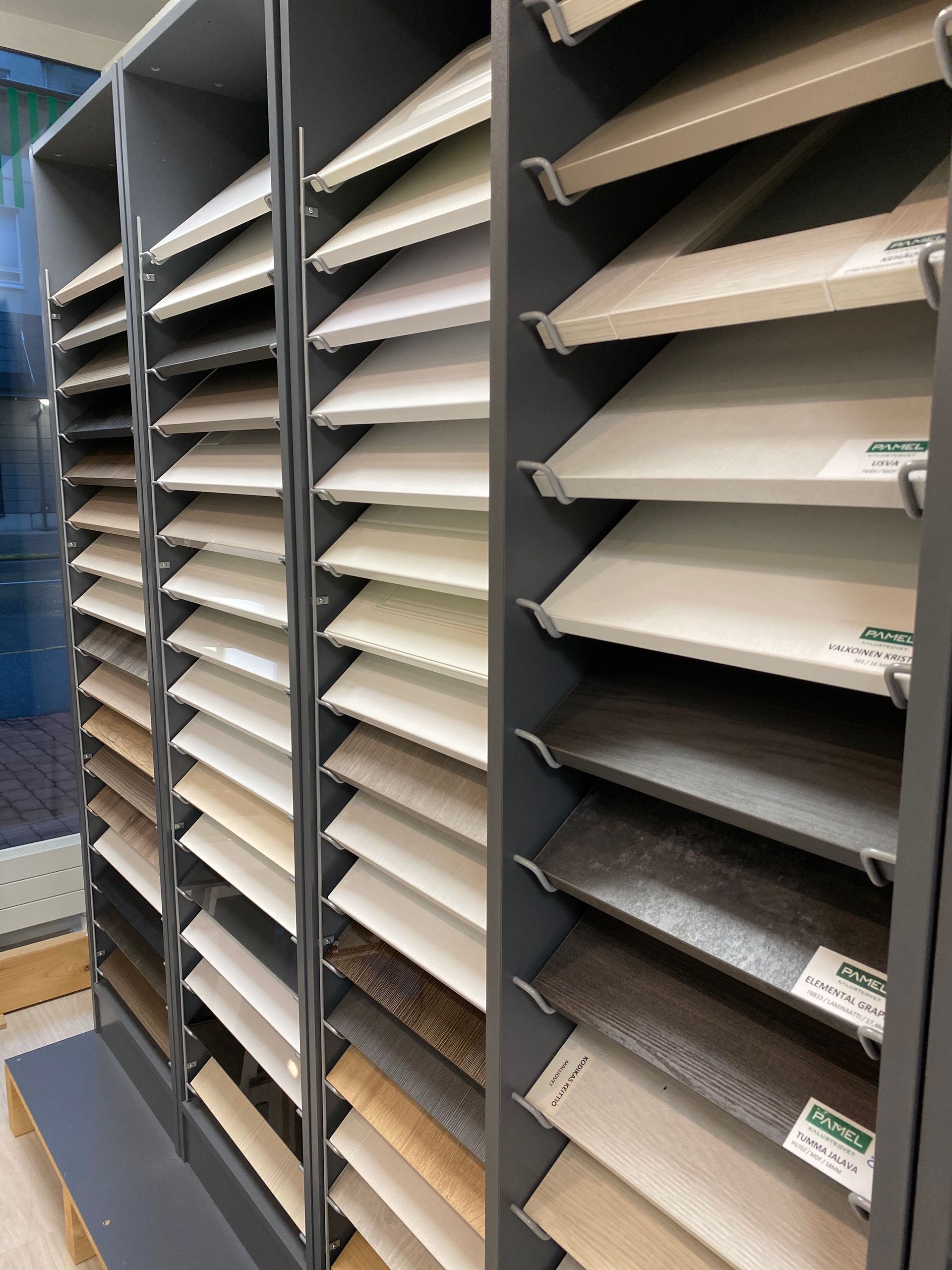 Erilaisten puu- tai laminaattinäytteiden esillepano vähittäismyymälässä, järjestettynä kulmikkaille hyllyille pystysuoraan esillepanoon.