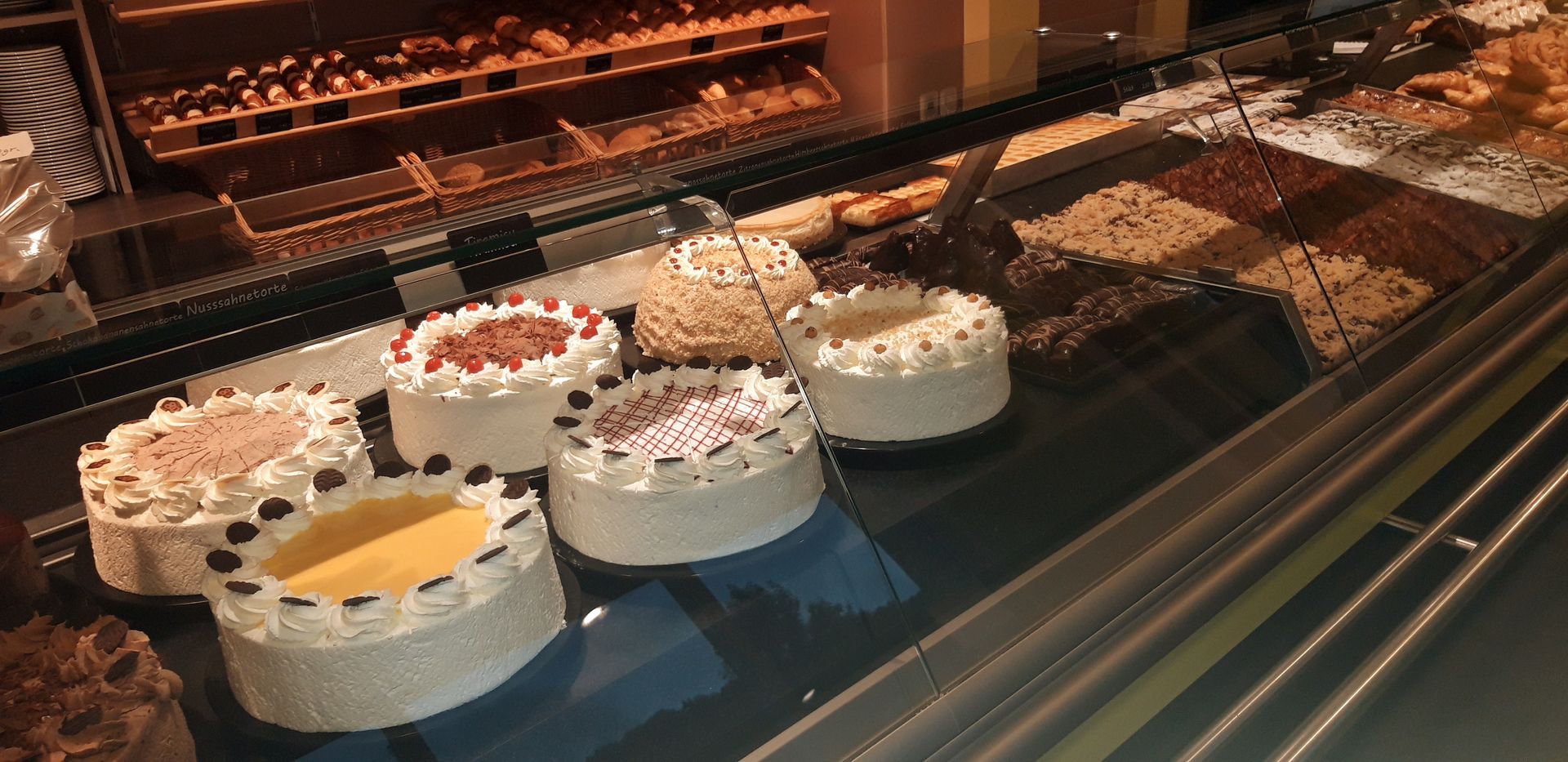 Reihen bunter Minikuchen in einer Vitrine, einige mit Obst- und Schokoladendekorationen.