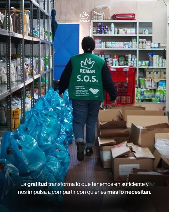 Una persona con un chaleco verde camina por un almacén lleno de pilas de botellas de agua y cajas.