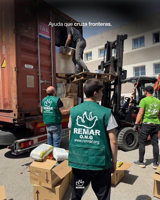 Voluntarios con chalecos verdes descargaban suministros donados de un camión a una carretilla elevadora frente a un edificio.