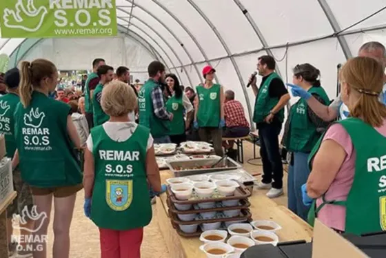 Voluntarios con chalecos verdes sirven comida bajo una carpa en un puesto de ayuda de REMAR SOS.