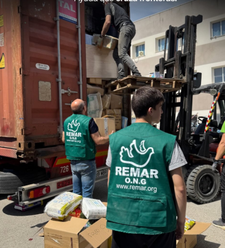 Voluntarios descargan cajas de un camión utilizando una carretilla elevadora junto a un contenedor de carga rojo.