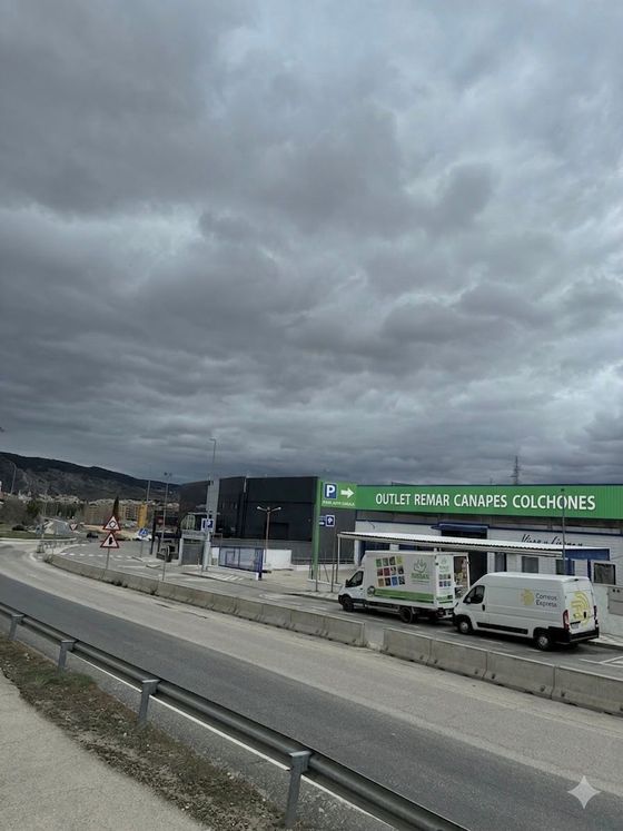 Un día nublado sobre un mercado al borde de la carretera con furgonetas blancas aparcadas y un letrero verde en la fachada de una tienda.