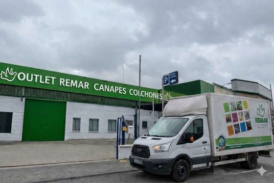 Camión de reparto blanco frente a una tienda outlet verde y blanca bajo un cielo nublado.